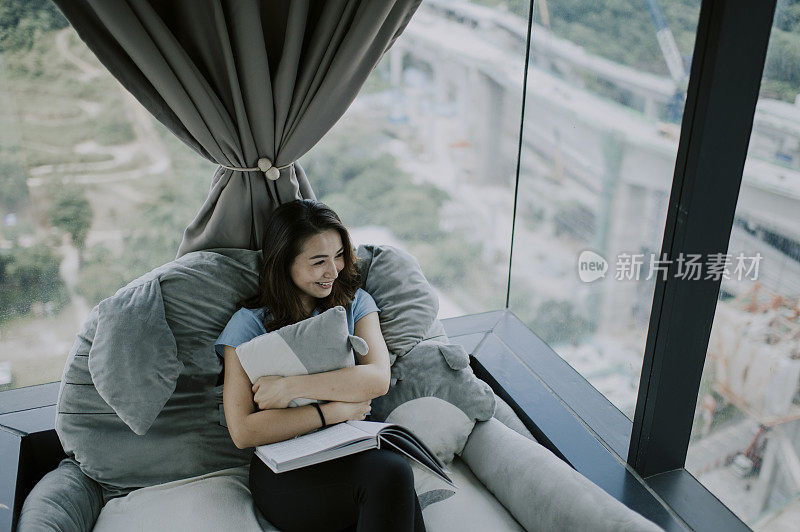 an asian chinese beautiful woman spending leisure time at the corner of her house reading book